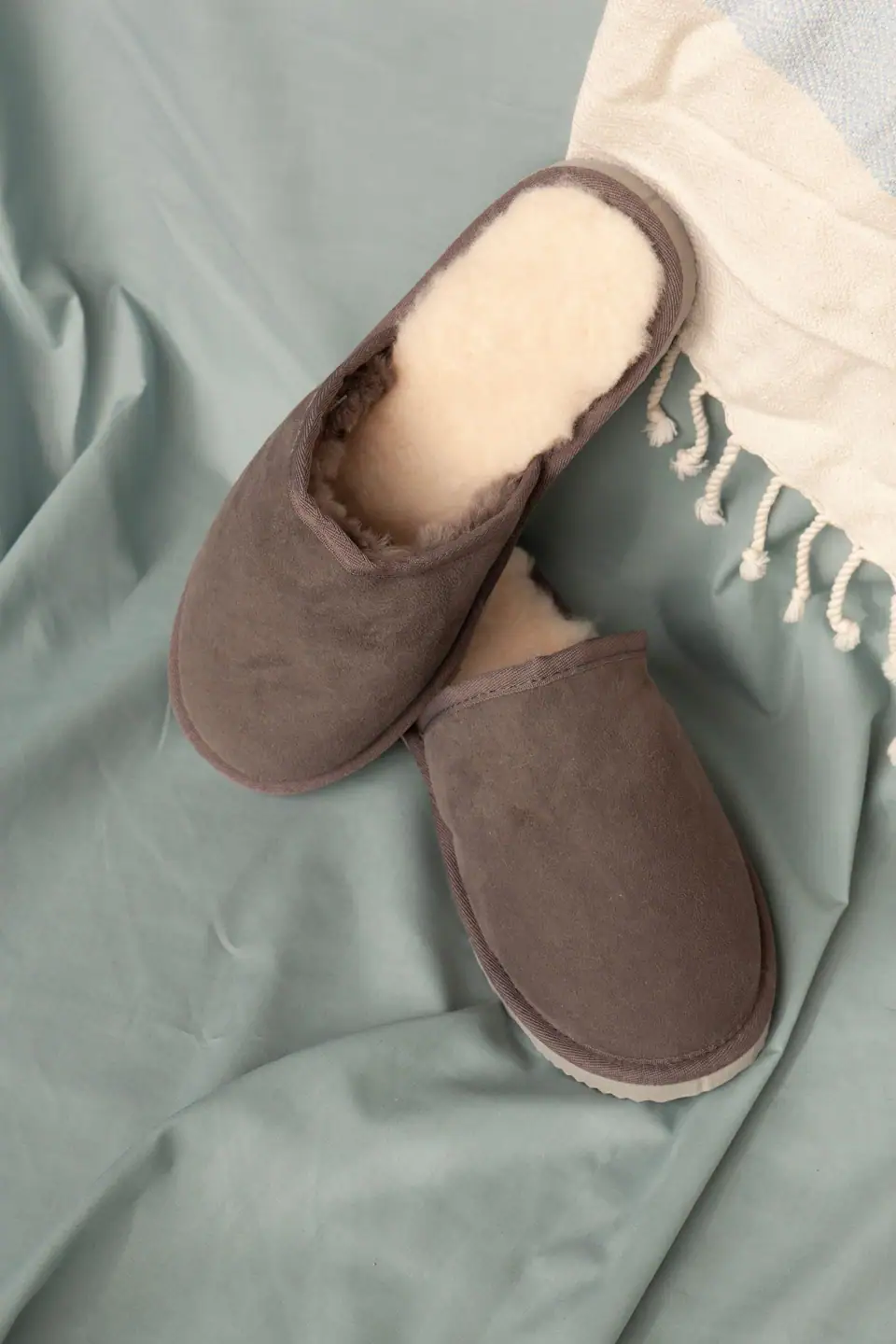 A pair of brown slippers with cream fleece lining resting on a soft blue throw