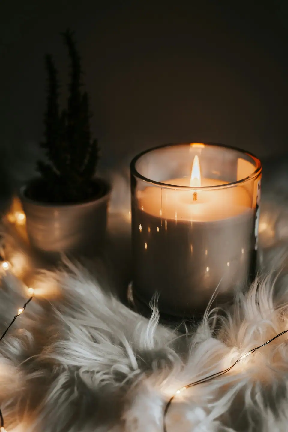 A lit candle in a glass jar beside a faux fur throw