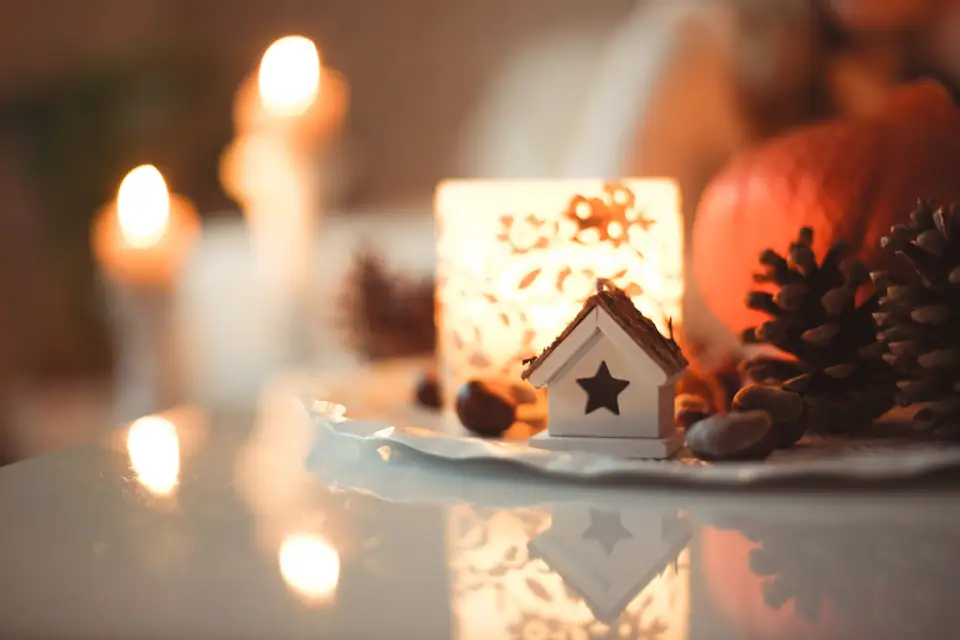 Lit candles and a small wooden house ornament with pine cones on a table