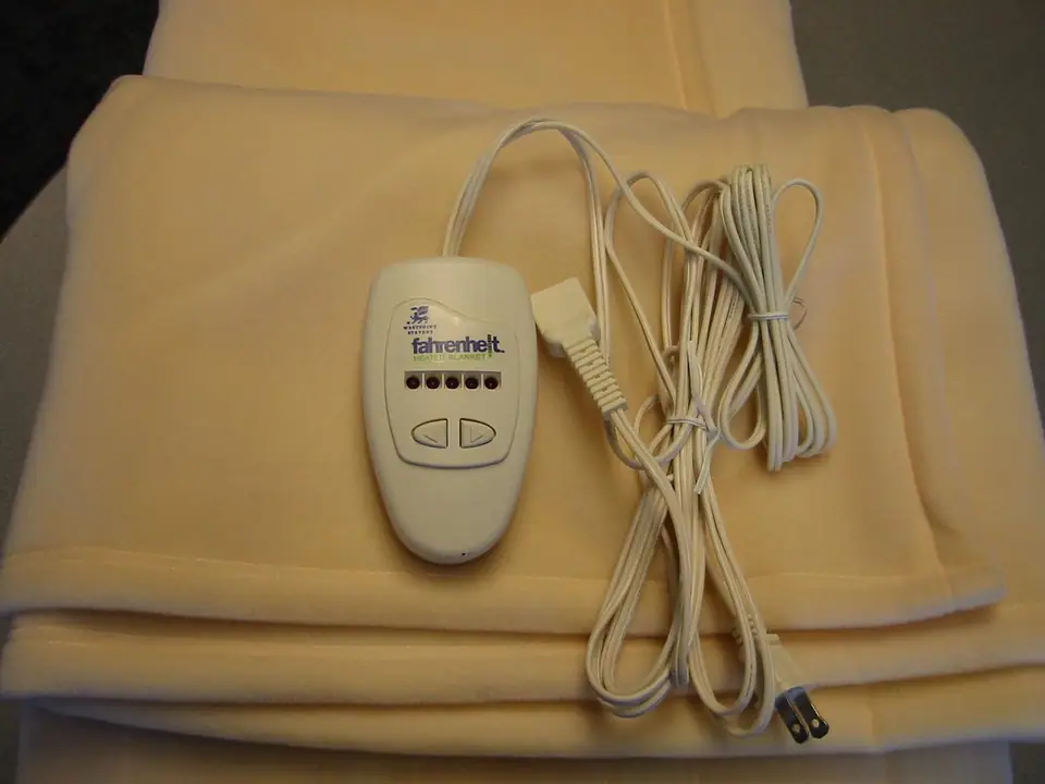 A cream fleece electric blanket folded with its plug-in hand controller and cord