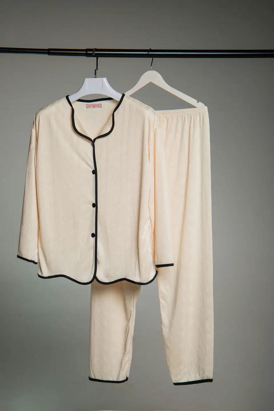 A cream pajama set with black piping hanging against a plain wall