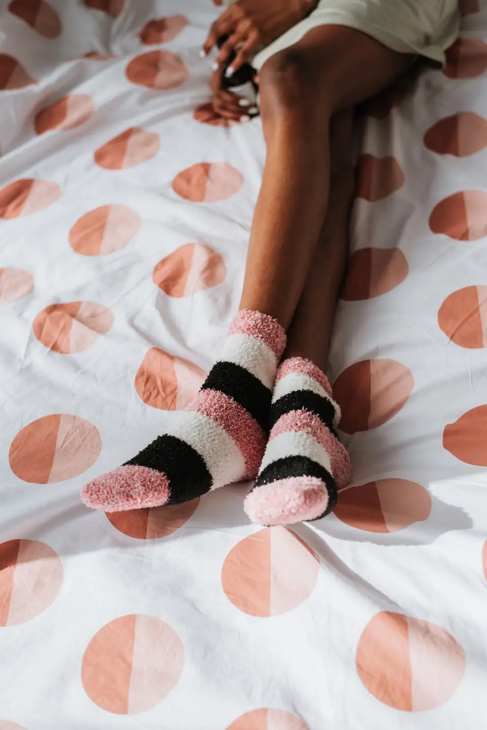 Feet in pink and black fuzzy socks crossed on a white duvet