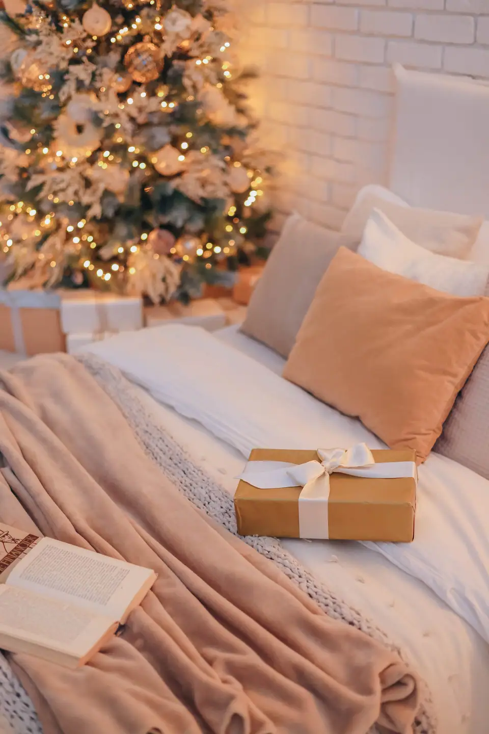A wrapped gift on soft bedding with pillows and a lit holiday tree behind