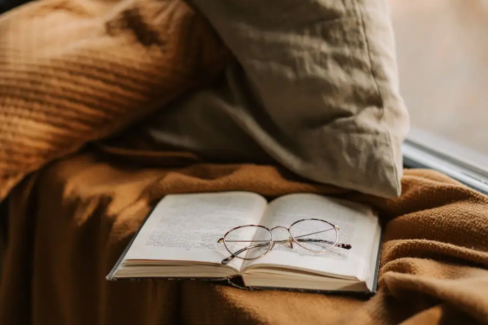 Reading glasses resting on an open book on a soft brown blanket