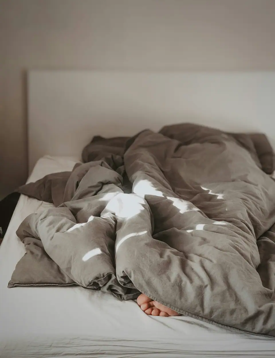 Rumpled grey and white bedding on an unmade bed