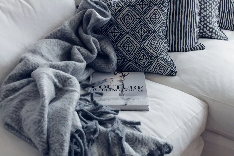 A soft grey faux fur throw draped over a white sofa with patterned cushions