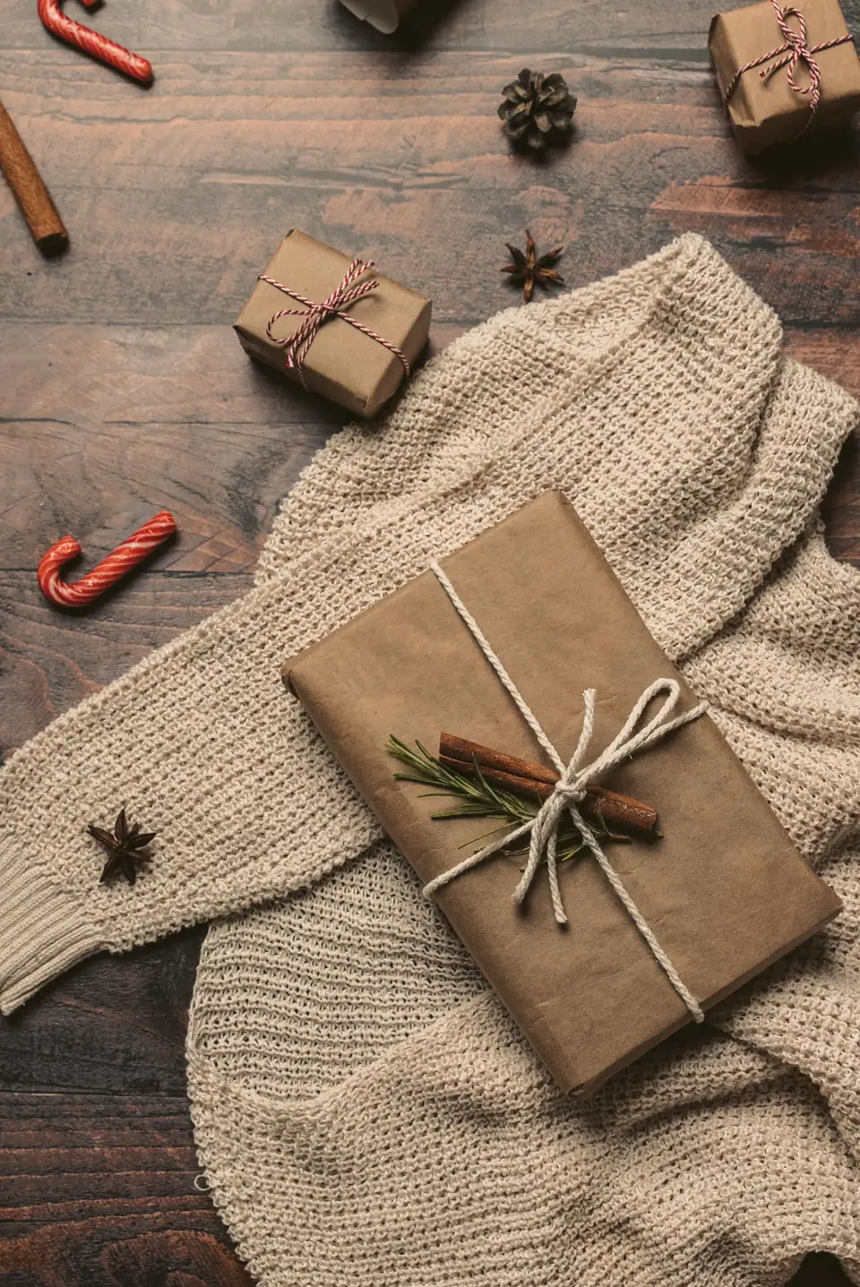 A kraft-paper gift tied with twine on a knitted throw with cinnamon sticks and a candy cane