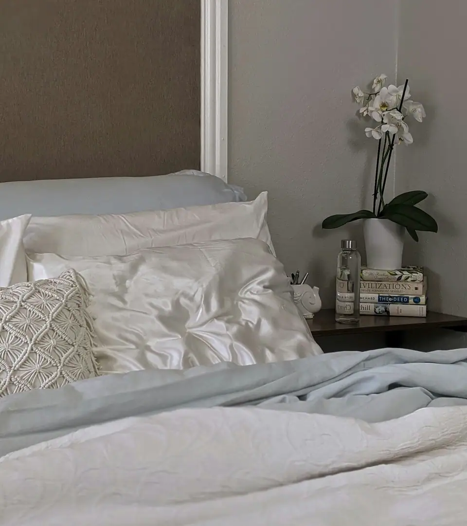Glossy satin pillowcases on a made bed beside a white orchid