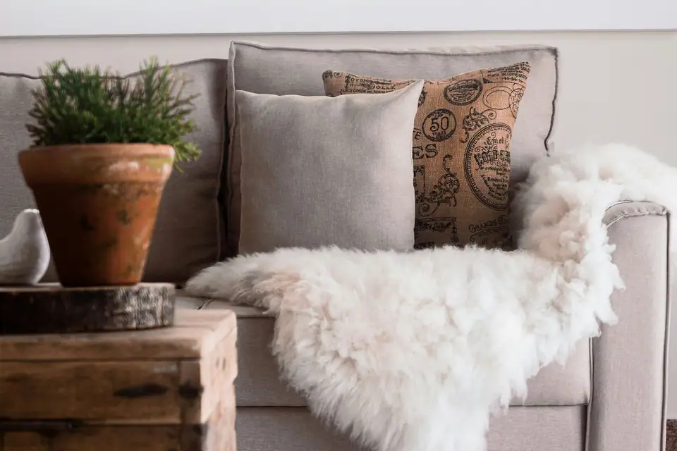 A fluffy white sheepskin throw and linen cushions on a beige sofa beside a potted plant
