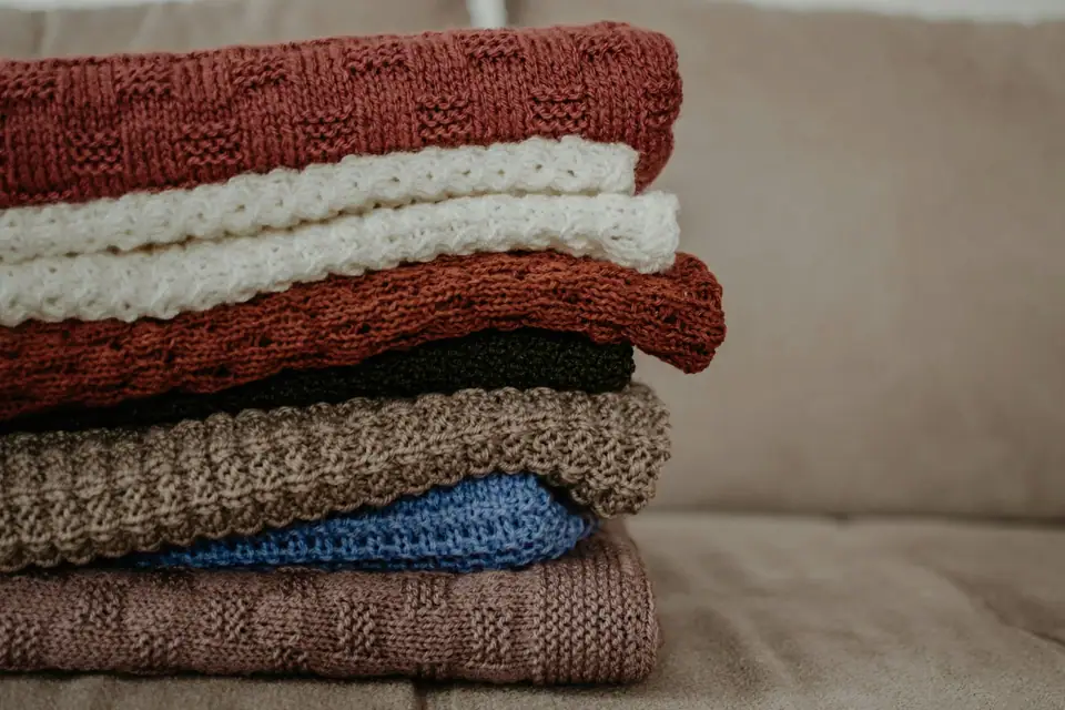 A stack of folded knit blankets in rust, cream and blue on a sofa