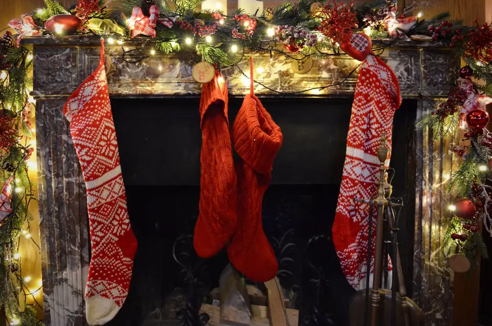 Red knit stockings hanging from a fireplace mantel with string lights