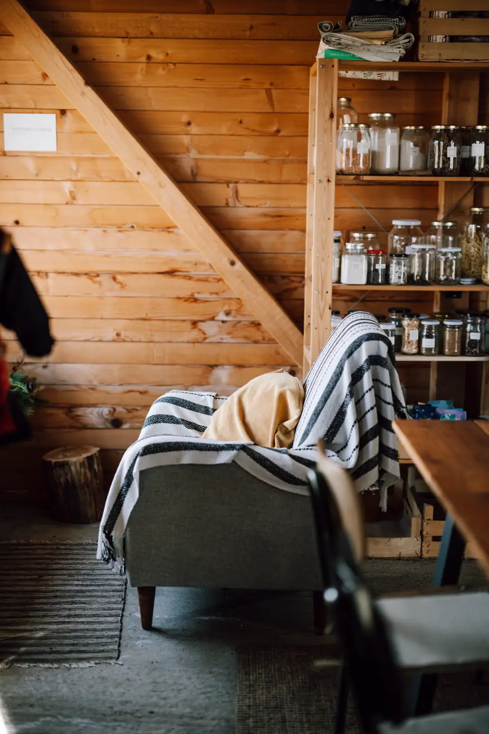 A striped woven throw draped over an armchair in a wood-paneled room with shelves of jars