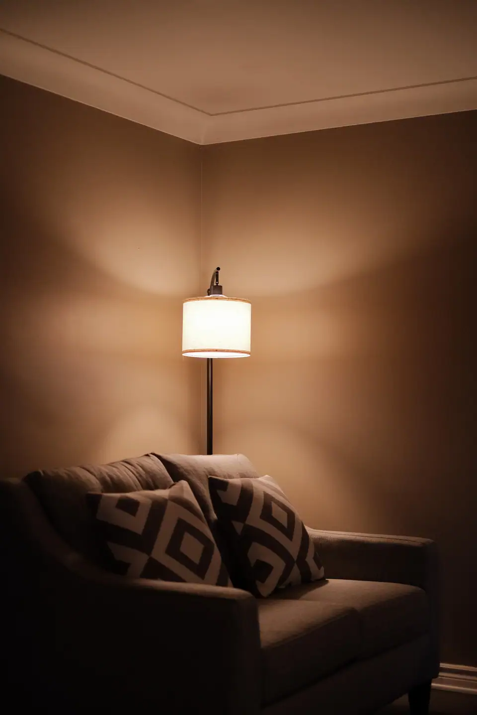 A living room corner lit by a warm table lamp, with a throw on the sofa