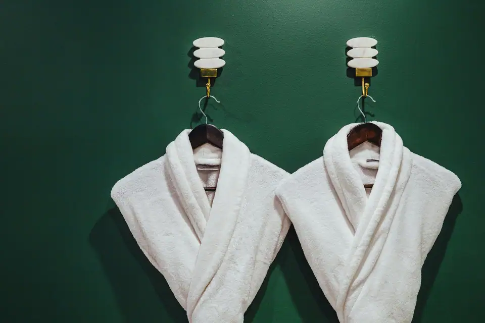 Two white plush robes hanging on hooks against a green wall