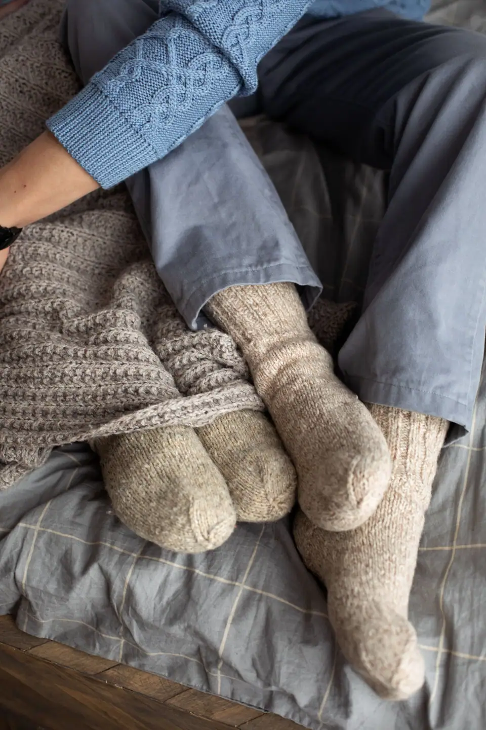 Feet in thick gray wool socks beside a knitted sweater on a bed