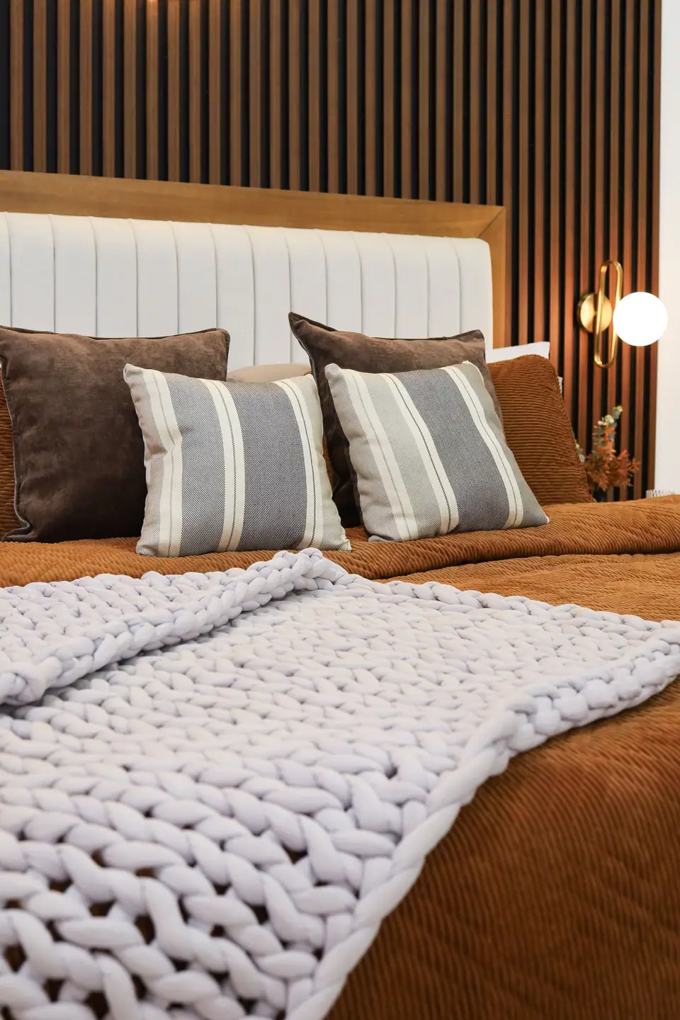 A chunky knit blanket over rust bedding with brown velvet and striped pillows